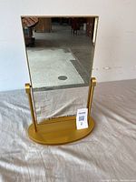 Front view of vintage Christian Dior swivel mirror showing rectangular reflective surface with branding on the bottom and gold-toned oval base.