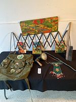 Antique expandable metal car luggage rack, vintage car light, green canvas Girl Scout backpack with various patches, several children's books, wooden golf club, small beaded pouch, and brush on black table.