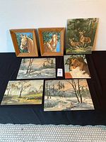 Overview of all seven paint by numbers paintings including two framed horse portraits and unframed paintings of deer, dog, and landscapes.