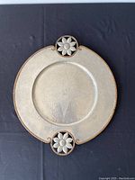 Top-down view of the circular pewter tray showing hammered texture and copper edged floral handles top and bottom.