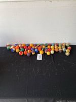 Wide shot showing the full assortment of over 50 vintage pool balls arranged on a black surface against a white wall.