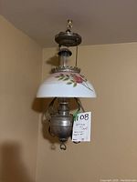 Full view of antique hanging oil lamp mounted on ceiling, showing floral glass shade and metal body