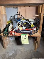 Photo showing a pile of various electrical cords and power strips on a wooden shelf with a yellow note marked '13 Electrical cords'
