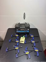 Full view of seven Irwin Quick-Grip clamps arranged on a black table with the XKONE carrying case in the back, labeled lot 21