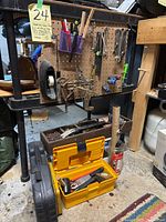 Photo of assorted hand tools hanging on a pegboard including wrenches, clamps, a saw, and boxes of nails and other fasteners, with a yellow toolbox and step stool below.