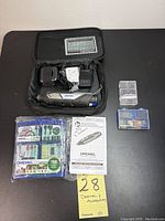 Top view of Dremel 8240 rotary tool in black soft carrying case along with battery charger, extra accessories, 160-piece Dremel accessory kit in sealed plastic packaging, smaller blue accessory case, and instruction manual lying on black surface.