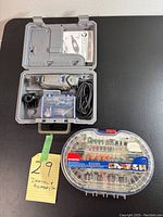 Dremel rotary tool model 3000 with power cord in gray carrying case, including small parts and manual; WorkPro accessory kit closed in transparent plastic case with red latch.