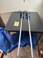 Top view of two 4 ft pipe clamps laid on a black table with some blue tarp and other objects partly visible around.
