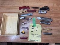 Wooden crate and all contents laid out on table including various pocket cutters and one lighter, total 16 items.