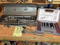 Metal toolbox with socket set and sanding drum set arranged on wooden surface.