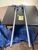 Two 4 ft long metal pipe clamps laid flat on black table, showing full length and blue clamp details.