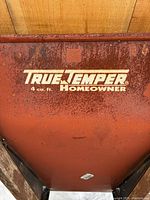 Close-up of rust-covered metal tray with True Temper Homeowner branding in white text indicating 4 cubic feet capacity.