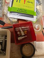 Drawer containing red tray with assorted cable connectors and cable ties, tape rolls