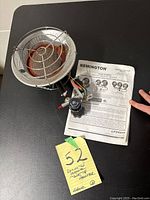 Photo of Remington propane tank top heater with attached control valve and instruction manual on a black surface, yellow sticky note with lot number.