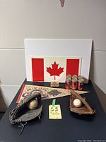 Two vintage baseball gloves each holding a baseball, Blue Jays pennant, six collectible cans, sealed card box, large Canadian flag poster board