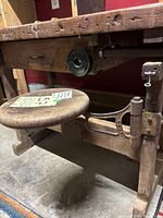 Side view of workbench showing wooden legs, attached swivel stool and vise support