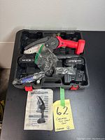 Photo of cordless mini chainsaw and accessories in carrying case, including batteries, charger, extra chain, oil can, screwdriver, and instruction manual.