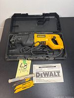 Full view of Dewalt DW310 reciprocating saw in black plastic carrying case with power cord coiled inside, instruction manual, three yellow Dewalt saw blades, and Millstar accessory in tube.
