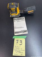 Dewalt cordless 1/4 sheet palm sander with dust collection bag and instruction manual on black surface.