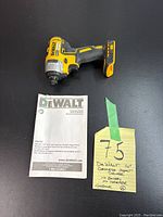 Photo showing Dewalt impact driver bare tool with no battery or charger, placed next to instruction manual and handwritten note describing the lot.