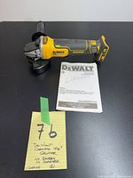 Front-left view of DeWalt DCG413 grinder with side handle and instruction manual alongside handwritten lot note.