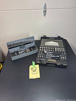 Photo showing Huot metal case of assorted drill bits alongside JobMate socket set case open with sockets and ratchets visible.
