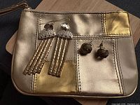 Two pairs of earrings displayed on metallic patchwork jewelry pouch; long hammered silver and gold tone dangle earrings and chunky knotted gold tone studs