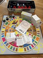 Game board laid out with cards, dice, card holders, and dispenser all visible inside a metal tin container.