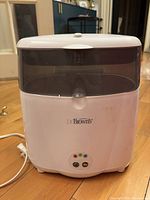 Front view of Dr. Brown's white bottle sterilizer with translucent gray lid and front panel, displaying buttons and indicator lights