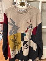 Full front view of the multicolor Bugs Bunny knit sweater hanging on a hanger, showing the full graphic patchwork design.