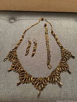 Set of black and gold beaded necklace, bracelet, and earrings laid out on a grey fabric surface
