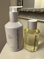 Both Dermalogica products together: White pump bottle of Body Hydrating Cream and clear bottle of Phyto Replenish Body Oil with silver cap.
