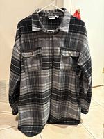 Front view of a black, gray and white plaid oversized women's shacket by Noisy May, showing zipper closure and two buttoned flap breast pockets.