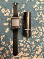 Black smartwatch next to black cylindrical PowerAdd Slim 2 power bank on patterned carpet.