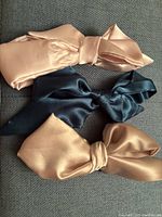 Photo of three tied hair ties in dusty rose, deep teal, and champagne, showing their bow style and smooth silk texture.