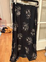Full view of the black vintage silk midi skirt with white floral outline print, hanging on a hanger against a door.