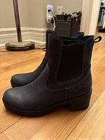 Side profile view of black Cougar waterproof winter boots with chunky heel and elastic side gussets on wood floor.