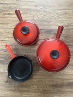Top view of two lidded pots and small frying pan, all with red exterior and black lid knobs on pots.