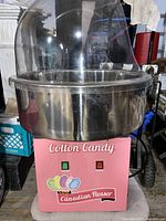 Front view of pink-bodied cotton candy machine with metal bowl and clear dome showing control switches and branding