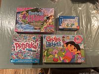 Four boxed children’s games and puzzle displayed on a surface, showing front box art of Disney Princess Surprise Slides, Dora the Explorer Chutes and Ladders, Hasbro Pictureka!, and a Disney puzzle.