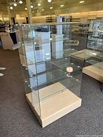 Fully assembled double-sided glass display case with wooden base on casters inside showroom.