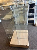 Front and side view of the glass display case showing glass shelves, wooden base on casters, and glass brackets.