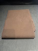 Chocolate brown flat sheet folded on dark fabric background.