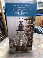 Box front showing image and name of the holiday lantern with LED light, snowman scene inside the lantern, in English and French and Spanish.