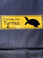 Single yellow "I brake for Turtles" car sticker on dark fabric background showing text and turtle graphic.