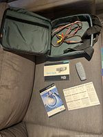 Open carrying case with AV cables inside, remote control and manuals laid out on a couch