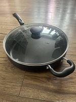 Top view of the large black T-Fal non-stick frying pan with glass lid on a wood floor.