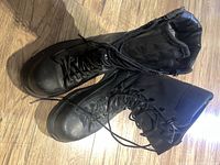 Top-down view of new black leather military boots with laces and side zippers, shown on wooden floor.
