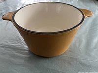 Yellow cast iron pot with white enamel interior shown from side angle showing shape and handles