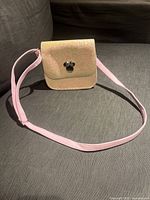 Front view of the glitter gold Minnie Mouse purse with adjustable pink strap laid flat on grey surface